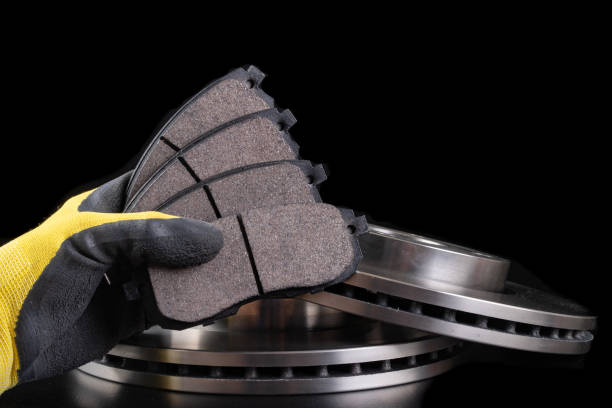 Brake pad for a passenger car in the hand of a mechanic. New spare parts for car repairs. Dark background.